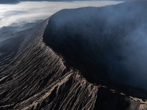 Aerial view of the rugged crater rim of Mount Bromo with volcanic ash and smoke rising from the caldera in Kecamatan Sukapura Jawa Timur Indonesia.