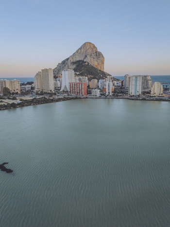 Aerial view of Penon de Ifach rising above the coastal town with high rise buildings and calm sea waters in Calp Valencian Community Spain. Aerial view of Penon de Ifach rising above the coastal town with high rise buildings and calm sea waters in Calp Valencian Community Spain.