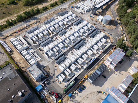 Aerial view of a large industrial battery energy storage facility with numerous white containers arranged in rows on a paved site in Poland.