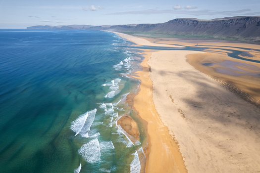 Aerial view of the vast Raudisandur beach with golden sand and turquoise waves along the coast of Vesturbyggd Iceland. Aerial view of the vast Raudisandur beach with golden sand and turquoise waves along the coast of Vesturbyggd Iceland.