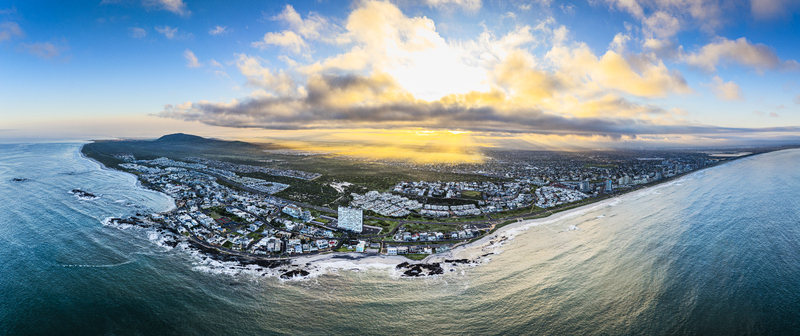 Aerial view of the Bloubergstrand coastline with sandy beaches and urban buildings under a golden sunset sky in Cape Town Western Cape South Africa.