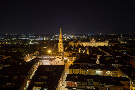 Aerial view of the illuminated Modena Cathedral and the Ghirlandina tower rising above the historic city center at night in Modena Emilia Romagna Italy.