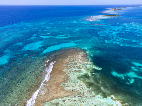 Aerial view of the vibrant coral reefs and turquoise waters surrounding the tropical island with small islets under a clear blue sky Guanaja Bay Islands Department Honduras. Aerial view of the vibrant coral reefs and turquoise waters surrounding the tropical island with small islets under a clear blue sky Guanaja Bay Islands Department Honduras.