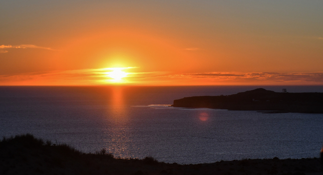 View of Puerto Piramides at sunset with the sun glowing over the calm ocean horizon and dark coastal cliffs Puerto Madryn Chubut Argentina. View of Puerto Piramides at sunset with the sun glowing over the calm ocean horizon and dark coastal cliffs Puerto Madryn Chubut Argentina.