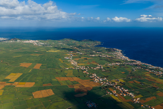 Aerial view of Pico Dona Joana geodesico overlooking lush green agricultural fields and coastal settlements along the blue Atlantic Ocean in Feteira Acores Portugal.