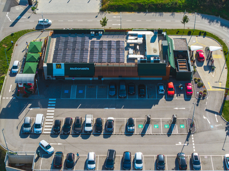 Aerial view of a McDonald s restaurant with solar panels on the roof surrounded by a parking lot with parked cars in Allhaming Oberosterreich Austria. Aerial view of a McDonald s restaurant with solar panels on the roof surrounded by a parking lot with parked cars in Allhaming Oberosterreich Austria.