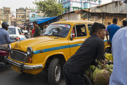View of a vibrant yellow taxi navigates bustling streets surrounded by vendors and pedestrians under the sun Kolkata West Bengal India. View of a vibrant yellow taxi navigates bustling streets surrounded by vendors and pedestrians under the sun Kolkata West Bengal India.