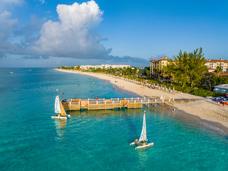 Aerial view of Grace Bay featuring a wooden pier two catamarans sailing in turquoise water white sandy beach and resort buildings in Grace Bay Caicos Islands Turks and Caicos Islands. Aerial view of Grace Bay featuring a wooden pier two catamarans sailing in turquoise water white sandy beach and resort buildings in Grace Bay Caicos Islands Turks and Caicos Islands.