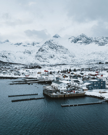 Aerial view of the village nestled between the dark tranquil waters and snow covered mountains Mefjordvær Troms Norway. Aerial view of the village nestled between the dark tranquil waters and snow covered mountains Mefjordvær Troms Norway.