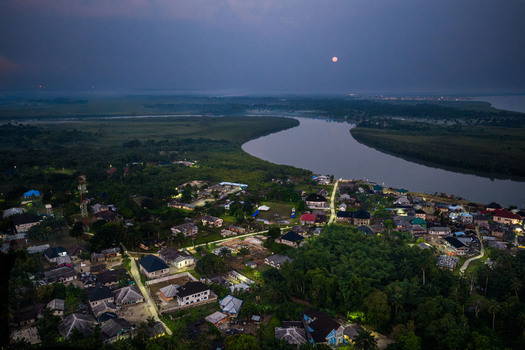 Aerial view of the town of Opobo nestled along the riverbank at dusk with lush vegetation and a full moon in the sky in Opobo Town Rivers Nigeria. Aerial view of the town of Opobo nestled along the riverbank at dusk with lush vegetation and a full moon in the sky in Opobo Town Rivers Nigeria.