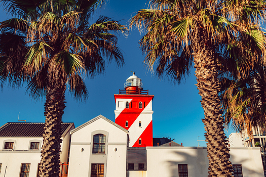 View of the red and white striped Green Point Lighthouse framed by palm trees under a clear blue sky in Cape Town Western Cape South Africa. View of the red and white striped Green Point Lighthouse framed by palm trees under a clear blue sky in Cape Town Western Cape South Africa.