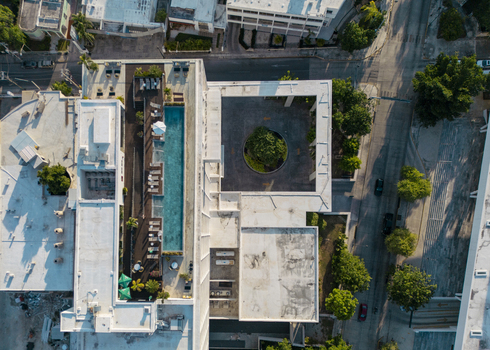 Aerial view of a modern building featuring a long rooftop swimming pool lounge chairs and a central courtyard with a tree in Merida Yucatan Mexico. Aerial view of a modern building featuring a long rooftop swimming pool lounge chairs and a central courtyard with a tree in Merida Yucatan Mexico.