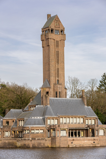 View of the Country Residence Museum Jachthuis Sint Hubertus with its iconic tall brick tower and slate roofs by the water in Hoenderloo Gelderland Netherlands.