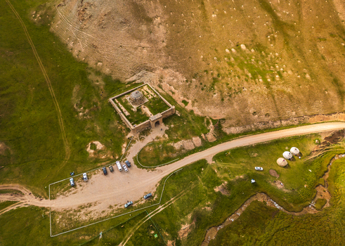Aerial view of Tash Rabat Caravan Palace surrounded by green grassy hills a dirt road a parking area with vehicles and traditional yurts in At Bashi District Naryn Region Kyrgyzstan. Aerial view of Tash Rabat Caravan Palace surrounded by green grassy hills a dirt road a parking area with vehicles and traditional yurts in At Bashi District Naryn Region Kyrgyzstan.