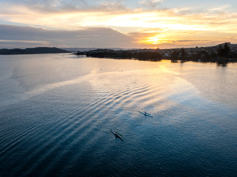 Raglan New Zealand 09 February 2026 Aerial view of two kayaks paddling on the calm waters of Raglan Harbour during a golden sunset with the coastal town visible in the distance.