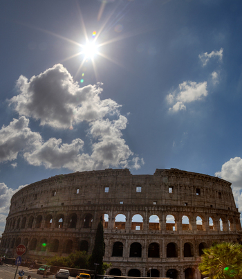 View of the Colosseum under a bright sunburst and blue sky in Roma Lazio Italy.