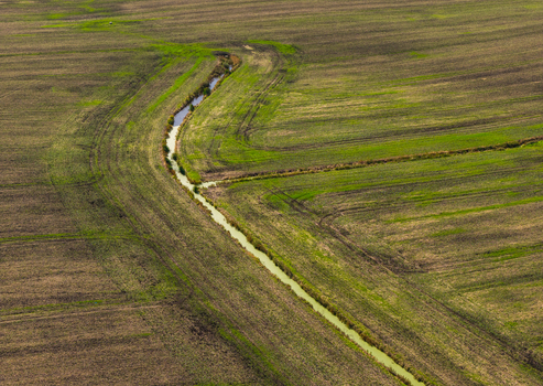 Aerial view of a winding stream flowing through agricultural fields in the Pomeranian Voivodeship Poland.