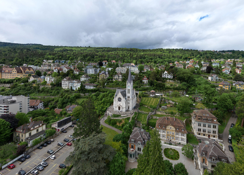 Aerial view of the historic St Mary s Church surrounded by lush green hills and residential buildings under a cloudy sky in Biel Bienne Canton of Bern Switzerland. Aerial view of the historic St Mary s Church surrounded by lush green hills and residential buildings under a cloudy sky in Biel Bienne Canton of Bern Switzerland.