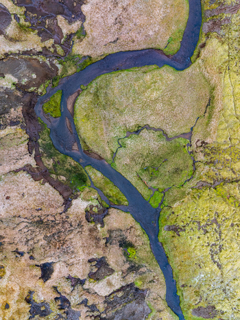 Aerial view of a winding river flowing through mossy volcanic terrain and marshland in Iceland. Aerial view of a winding river flowing through mossy volcanic terrain and marshland in Iceland.