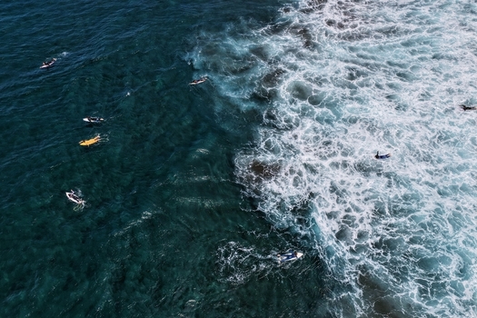 Aerial view of surfers waiting for waves at Praia do Areal de Santa Barbara with white foam and deep blue water in Ribeira Grande Acores Portugal. Aerial view of surfers waiting for waves at Praia do Areal de Santa Barbara with white foam and deep blue water in Ribeira Grande Acores Portugal.