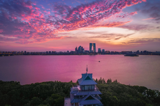 Aerial view of the Gate to the East skyscraper and Jinji Lake skyline under a vibrant pink sunset with a traditional pavilion in the foreground in Suzhou Jiangsu China.