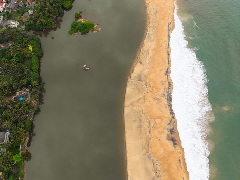 Aerial view of a narrow golden sandbar separating a calm river from the turquoise ocean waves and lush tropical palm trees in Galle Southern Province Sri Lanka. Aerial view of a narrow golden sandbar separating a calm river from the turquoise ocean waves and lush tropical palm trees in Galle Southern Province Sri Lanka.