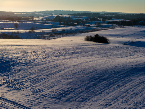 Aerial view of snow covered rolling hills and fields under a low winter sun with long shadows and distant forests in Lithuania. Aerial view of snow covered rolling hills and fields under a low winter sun with long shadows and distant forests in Lithuania.