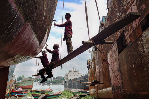Keraniganj Bangladesh 11 September 2022 View of workers repairing a large rusty ship hull while standing on a narrow wooden plank at Shipyard Dhaka.