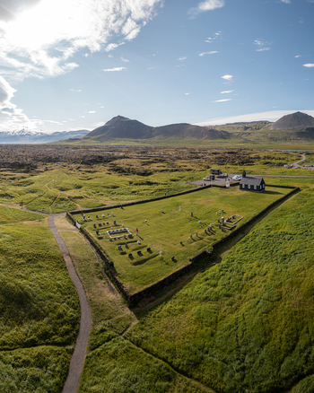 Aerial view of the historic black wooden Budakirkja church surrounded by a stone walled cemetery and vast green lava fields under a bright sky in Budir Snaefellsbaer Iceland. Aerial view of the historic black wooden Budakirkja church surrounded by a stone walled cemetery and vast green lava fields under a bright sky in Budir Snaefellsbaer Iceland.