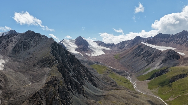 Aerial view of Engilchek Glacier surrounded by rugged mountain peaks rocky slopes and green alpine valleys under a clear blue sky in Ak Su Issyk Kul Region Kyrgyzstan. Aerial view of Engilchek Glacier surrounded by rugged mountain peaks rocky slopes and green alpine valleys under a clear blue sky in Ak Su Issyk Kul Region Kyrgyzstan.