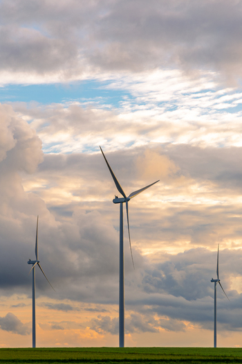 View of wind turbines standing in a green field under a dramatic cloudy sky during golden hour in Poland.