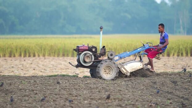 View of a farmer operating a power tiller in a field Bangladesh. View of a farmer operating a power tiller in a field Bangladesh.
