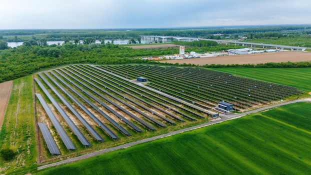 Aerial view of a large solar farm with rows of photovoltaic panels surrounded by green fields and a river with a bridge in the distance Sabac Vojvodina Serbia.