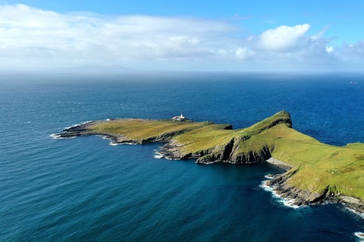 Aerial view of Neist Point Lighthouse on the rugged green cliffs of the Isle of Skye surrounded by the deep blue waters of the Atlantic Ocean in Isle of Skye Scotland United Kingdom.
