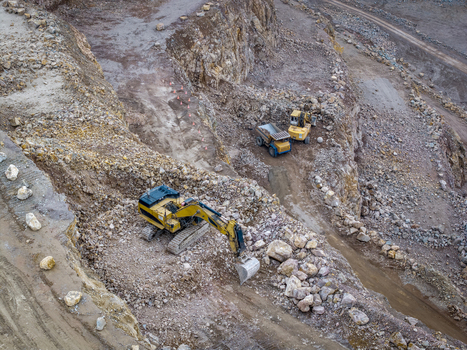 Aerial view of Porphyry Mine Zalas featuring a yellow excavator working on rocky terrain alongside heavy dump trucks in an open pit quarry. Frywald Wojewodztwo Malopolskie Poland.