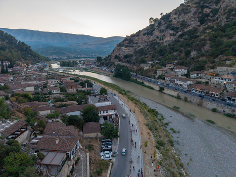 Aerial view of the historic city of Berat with traditional stone houses and terracotta rooftops lining the Osum River featuring a stone bridge and a road in Berat Berat County Albania.