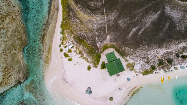Aerial view of Los Roques archipelago featuring white sand turquoise water a green roofed building small boats and umbrellas in Los Roques Dependencias Federale Venezuela. Aerial view of Los Roques archipelago featuring white sand turquoise water a green roofed building small boats and umbrellas in Los Roques Dependencias Federale Venezuela.