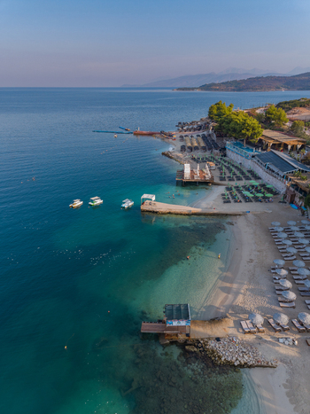 Aerial view of the turquoise waters and sandy beach of Ksamil with sun loungers small boats and coastal vegetation in Ksamil Vlore County Albania. Aerial view of the turquoise waters and sandy beach of Ksamil with sun loungers small boats and coastal vegetation in Ksamil Vlore County Albania.