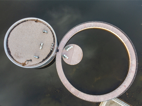 Aerial view of two circular structures connected by a winding path over dark waters creating a serene contrast of shapes and textures Utopia Flevoland Netherlands.