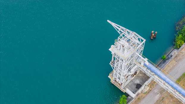 Aerial view of an industrial bulk loading tower with an enclosed conveyor system situated on the turquoise waters of the Rhone River in Le Pouzin Auvergne Rhone Alpes France.