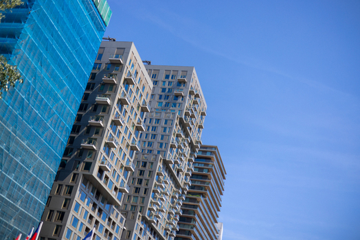 View of modern residential skyscrapers with balconies and a building under construction with blue safety netting under a clear blue sky in Rotterdam South Holland Netherlands. View of modern residential skyscrapers with balconies and a building under construction with blue safety netting under a clear blue sky in Rotterdam South Holland Netherlands.