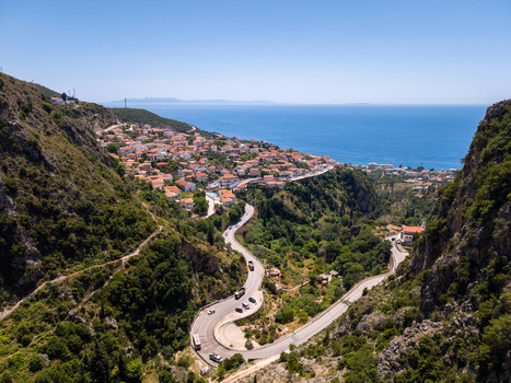Aerial view of the coastal village with red roofed houses and a winding mountain road leading towards the blue Ionian Sea in Dhermi Vlore County Albania.