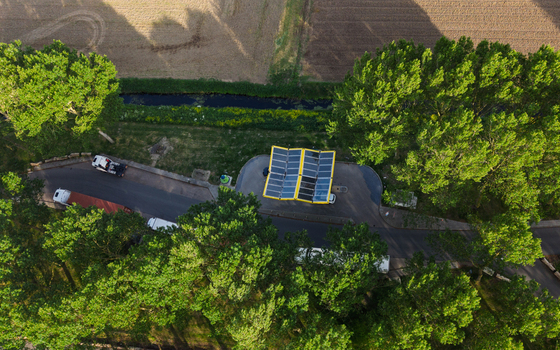 Aerial view of the Fastned Charging Station with its yellow solar panel roof nestled among lush green trees and fields in Vierpolders Zuid Holland Netherlands. Aerial view of the Fastned Charging Station with its yellow solar panel roof nestled among lush green trees and fields in Vierpolders Zuid Holland Netherlands.