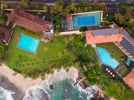 Aerial view of Gintota beach resort featuring turquoise swimming pools a blue tennis court and lush palm trees along the coastline in Galle Southern Province Sri Lanka. Aerial view of Gintota beach resort featuring turquoise swimming pools a blue tennis court and lush palm trees along the coastline in Galle Southern Province Sri Lanka.