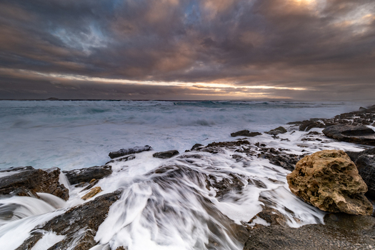 View of the rugged coastline at Sandpatch with waves crashing against rocky shores under a dramatic cloudy sky at sunset in Sandpatch Western Australia Australia. View of the rugged coastline at Sandpatch with waves crashing against rocky shores under a dramatic cloudy sky at sunset in Sandpatch Western Australia Australia.