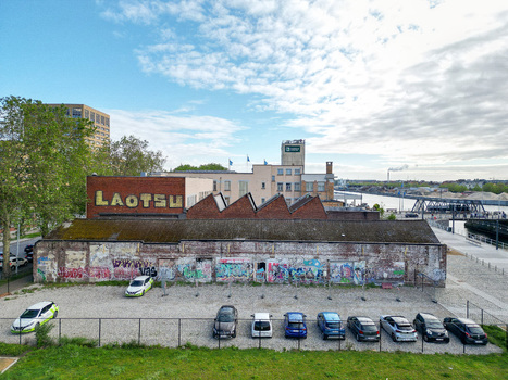Aerial view of an industrial brick building with graffiti and the word Laotsu on the facade next to a parking lot and a canal under a bright sky Brussels Brussels Belgium.