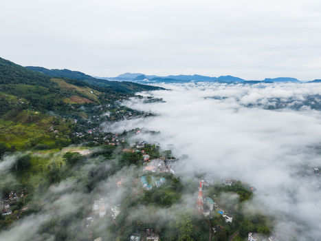 Aerial view of a town nestled in lush green hills partially covered by thick white clouds and morning mist under an overcast sky Kandy Central Province Sri Lanka. Aerial view of a town nestled in lush green hills partially covered by thick white clouds and morning mist under an overcast sky Kandy Central Province Sri Lanka.