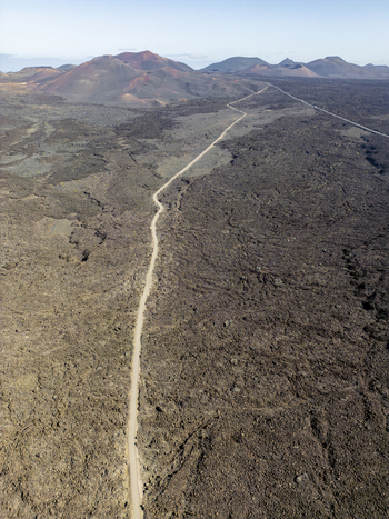 Aerial view of a long straight road cutting through the dark volcanic lava fields of Timanfaya National Park in Lanzarote Canarias Spain. Aerial view of a long straight road cutting through the dark volcanic lava fields of Timanfaya National Park in Lanzarote Canarias Spain.
