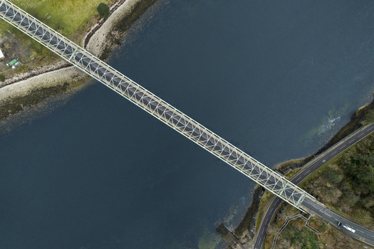 Aerial view of Ballachulish Bridge spanning the dark blue waters of Loch Leven with surrounding green banks and coastal roads Ballachulish Scotland United Kingdom.