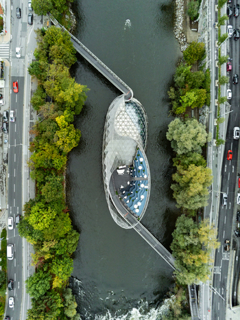 Aerial view of the Murinsel a modern floating island structure on the Mur river surrounded by lush trees and urban roads in Graz Styria Austria.